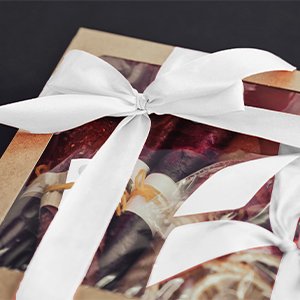 Gift box tied with white satin ribbon bows, showing contents through clear window.