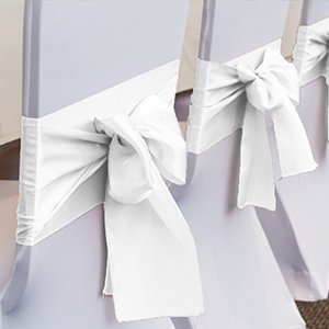 White satin ribbon tied into bows on the backs of two chairs, showing wedding decor.
