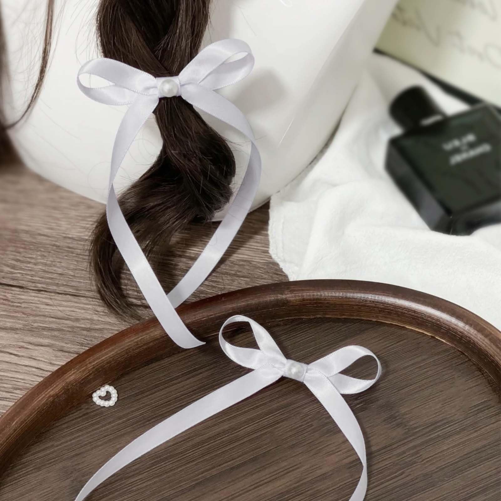 White satin ribbon bows with pearl accents tied in a braid and on a wooden tray