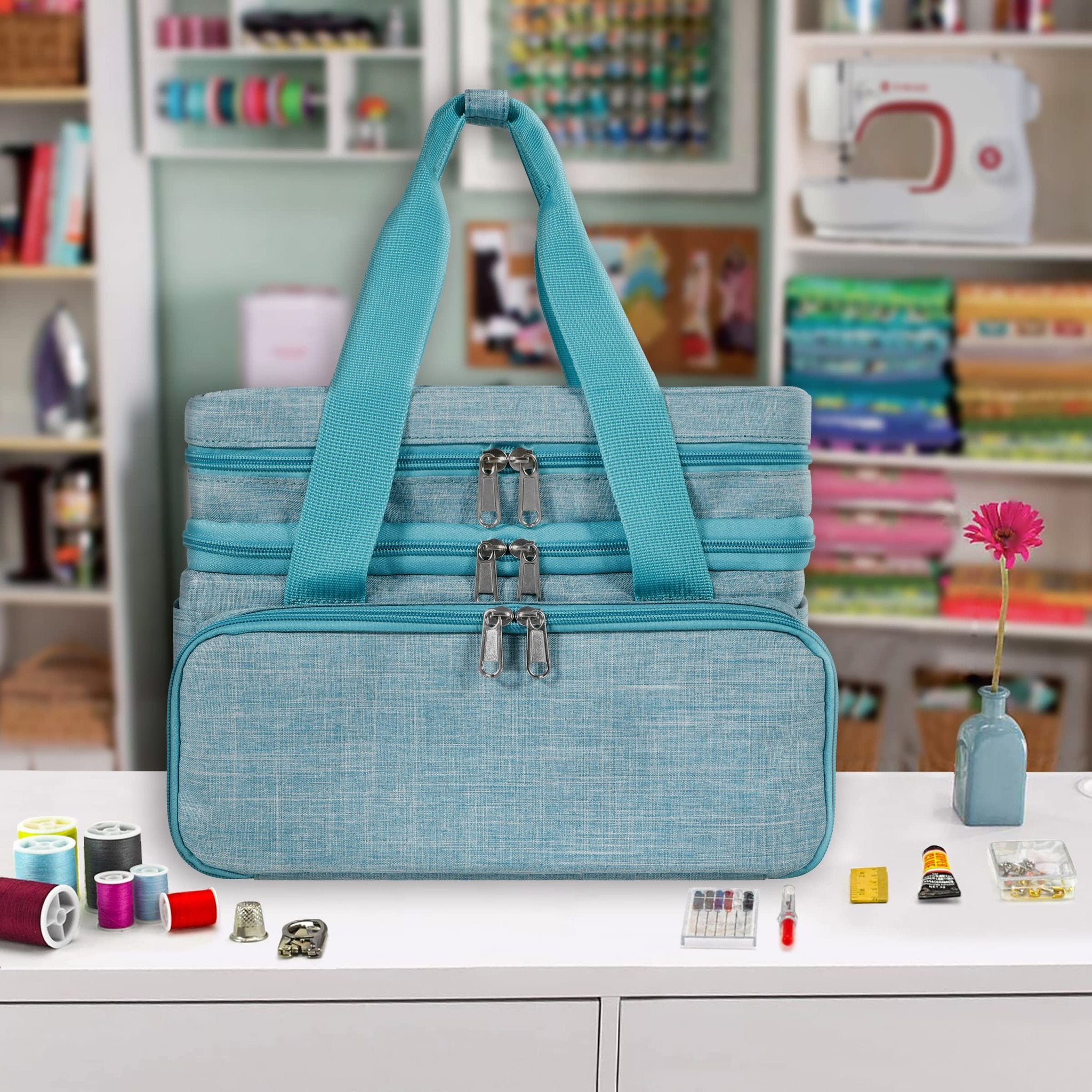 Teal sewing storage bag with multiple compartments and zippers, displayed on a white surface with sewing supplies.