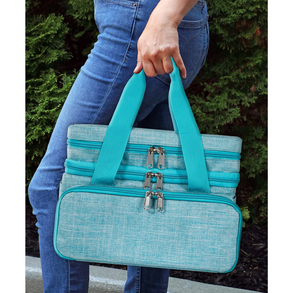 Person in jeans holding a teal double-layer sewing storage bag with multiple zippers outdoors.