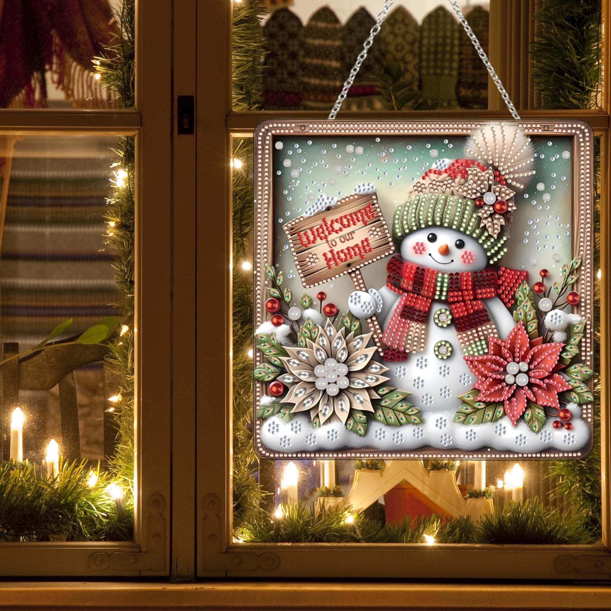 Diamond art snowman ornament hanging on a window with Christmas lights and garland