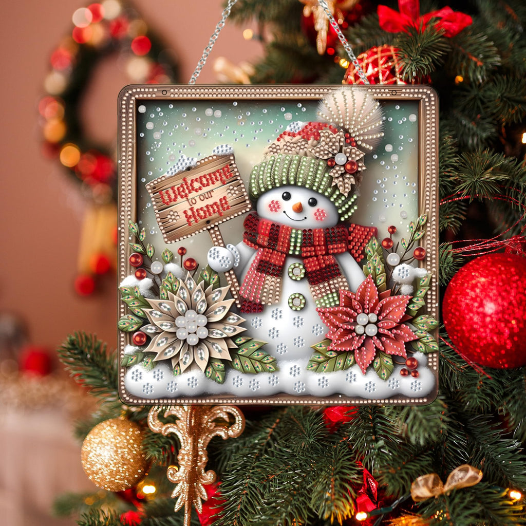 Diamond art snowman ornament with 'Welcome to our Home' sign hanging on a Christmas tree.