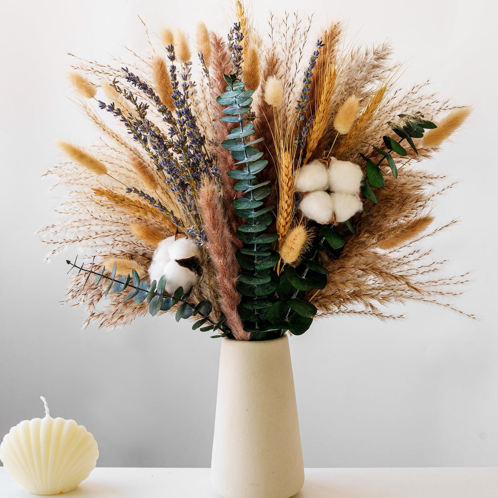 Dried flower bouquet with pampas grass, lavender, eucalyptus, and cotton stems in a vase, with a shell candle beside it.