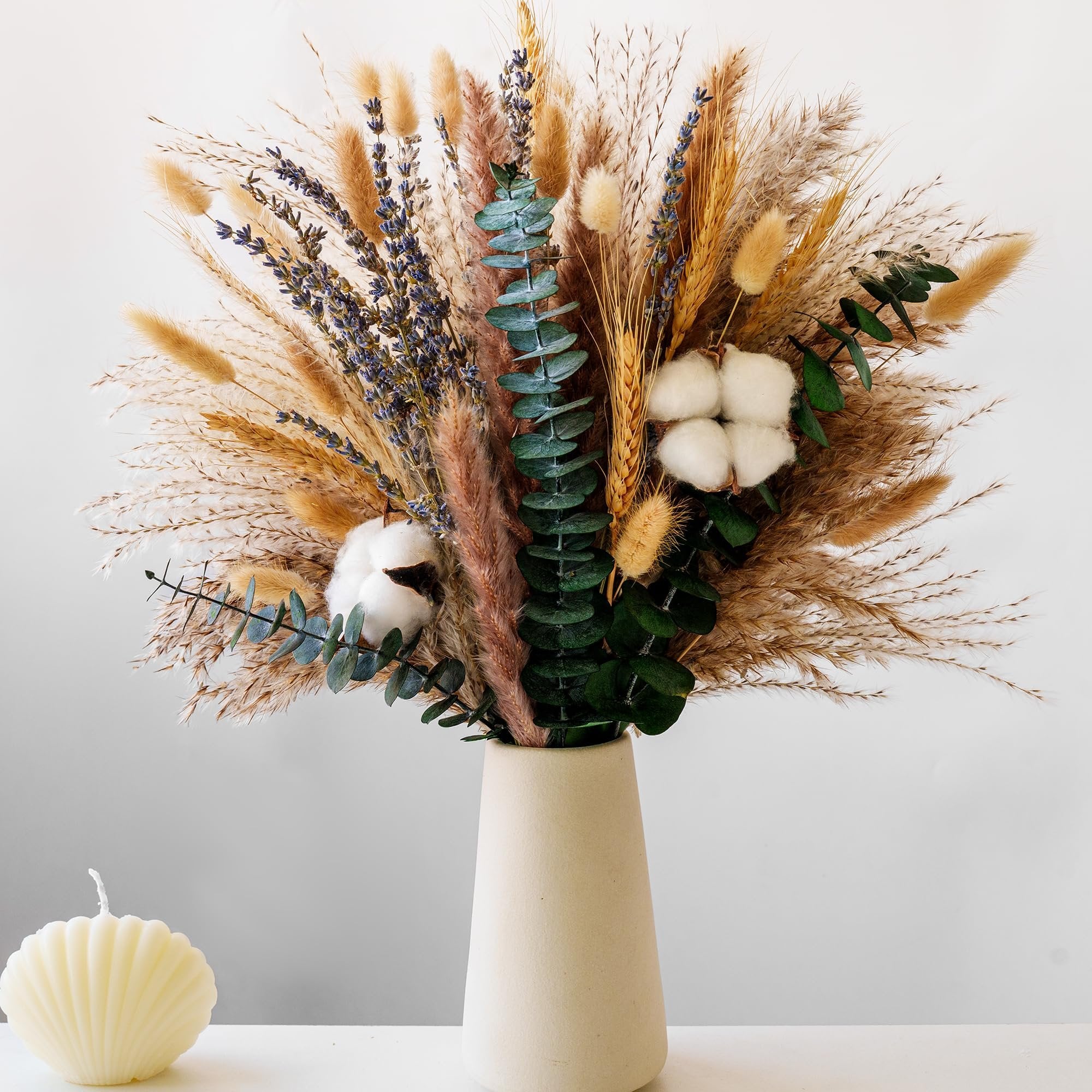 Dried flower bouquet with pampas grass, lavender, eucalyptus, and cotton stems in a vase, with a shell candle beside it.