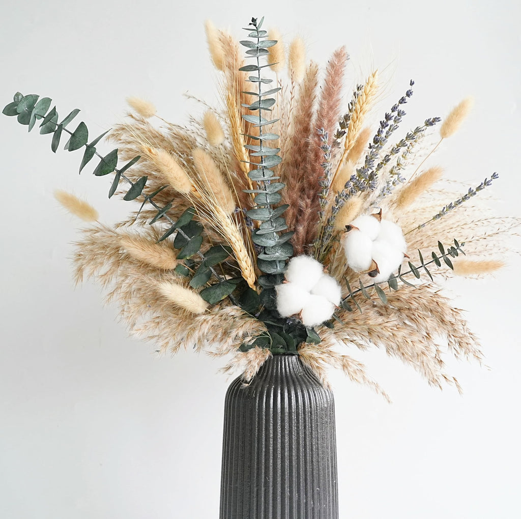 Dried flower bouquet with pampas grass, eucalyptus, cotton stems, and lavender in a ribbed vase against a white background.