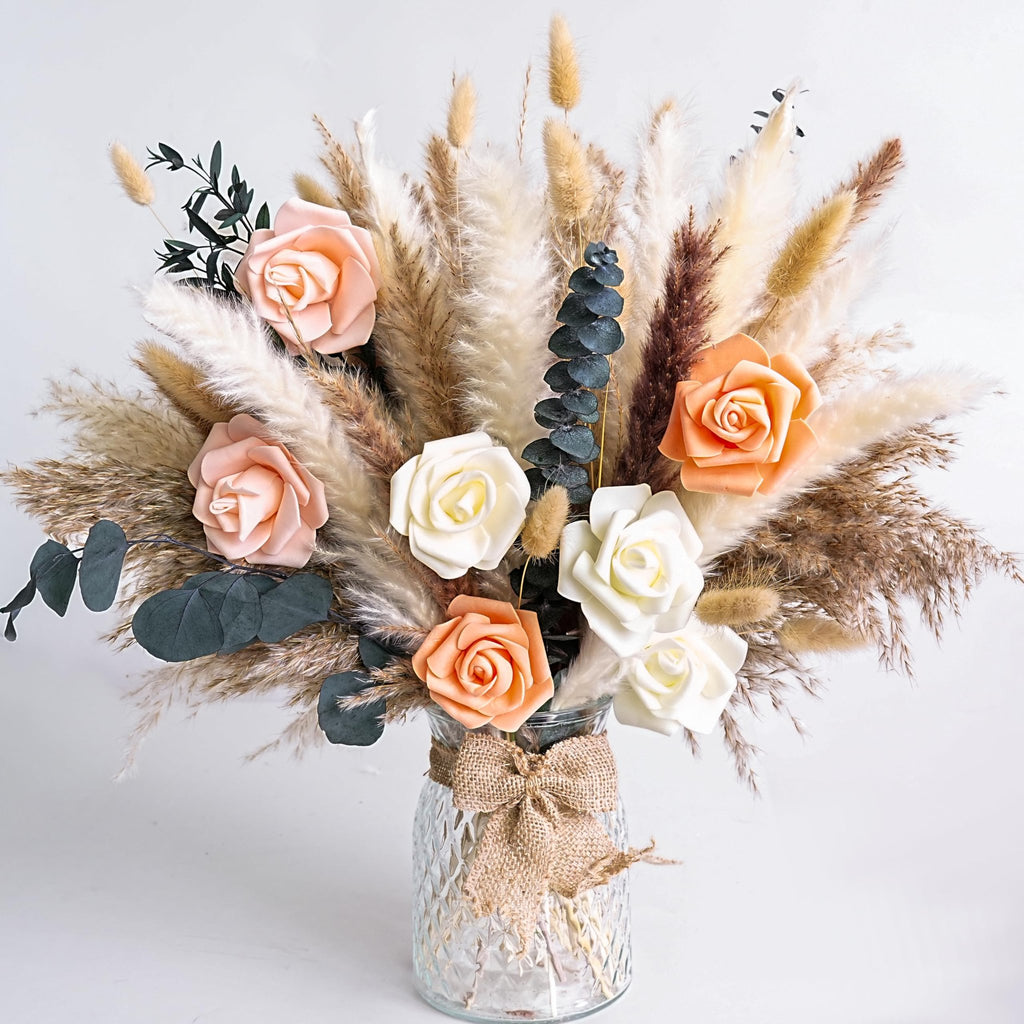 Dried flower bouquet with pampas grass and faux roses in a textured glass vase tied with burlap ribbon.