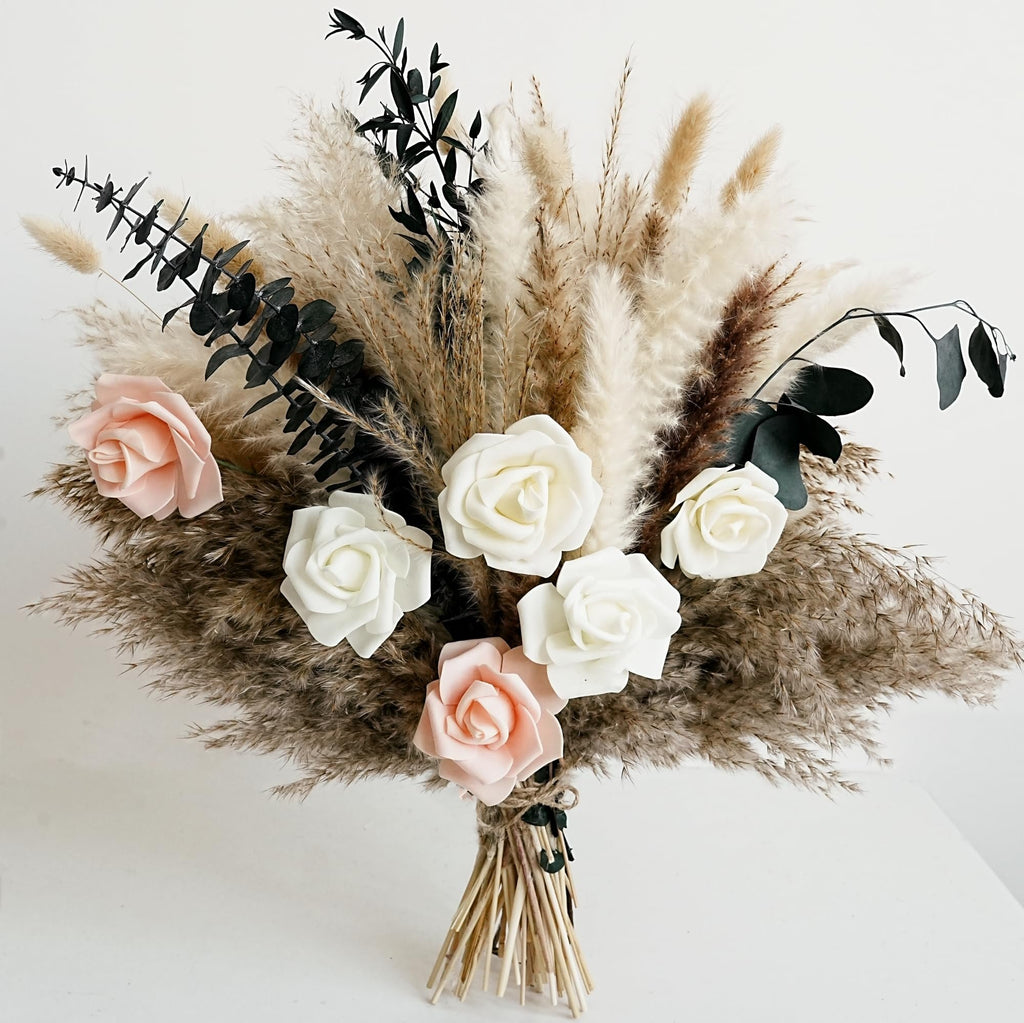 Dried flower bouquet with pampas grass, white and pink roses, and dark eucalyptus leaves, tied with twine.