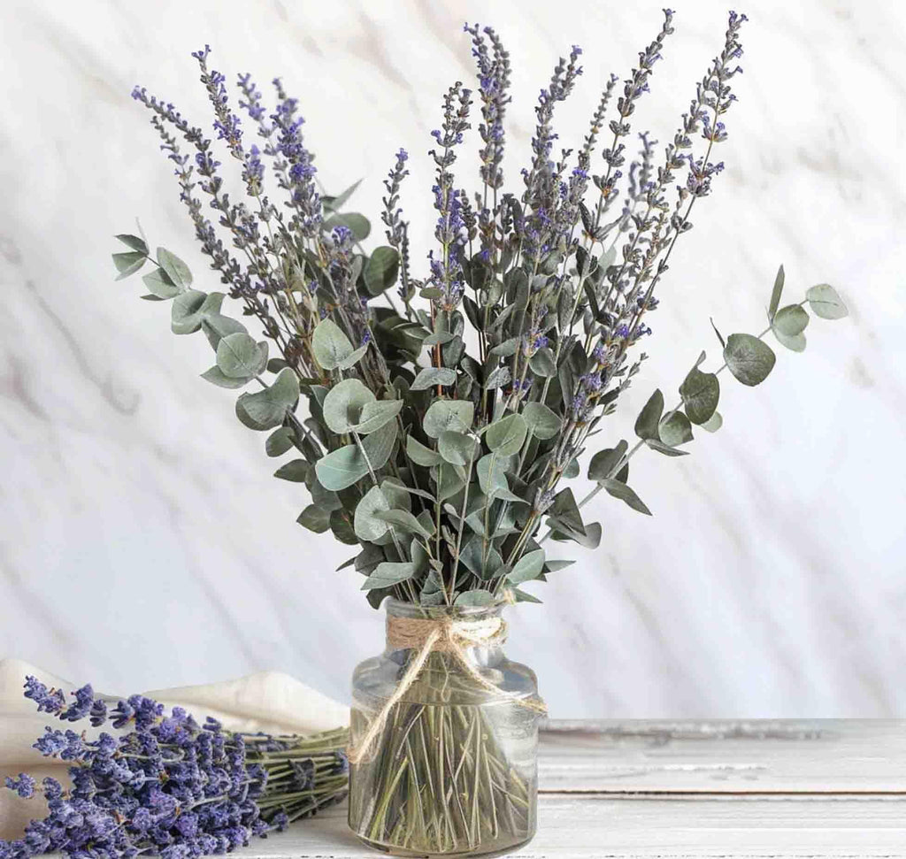 Dried lavender and eucalyptus bouquet in a glass vase with twine, and a separate bunch of lavender on a white cloth.