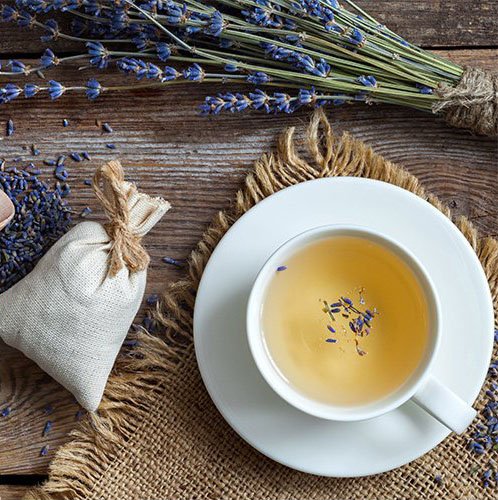 Cup of lavender tea with dried lavender sprigs and a sachet on a wooden table