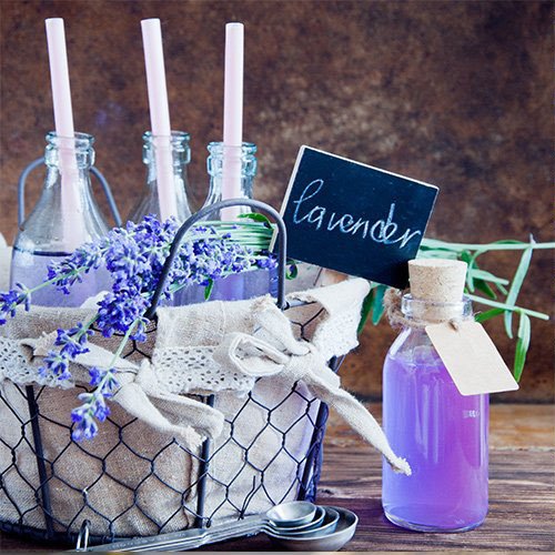 Lavender sprigs and purple liquid in bottles arranged in a rustic basket with a small chalkboard sign.