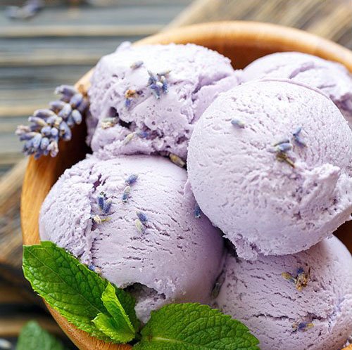 Scoops of lavender ice cream in a wooden bowl with fresh mint and lavender sprigs.
