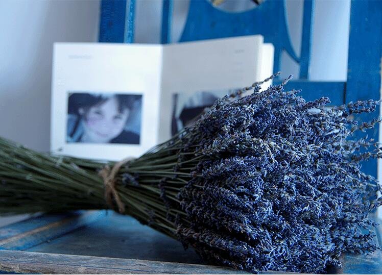 Bouquet of dried ultra blue lavender stems tied with twine, with an open booklet featuring child photos in the background.