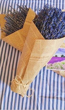 Two bouquets of dried lavender flowers wrapped in brown paper with text, tied with twine, on a striped blue and white cloth.