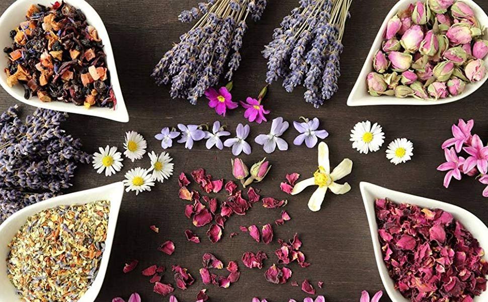 Dried lavender bundles and various dried flowers and petals arranged in white dishes on a dark wooden surface.