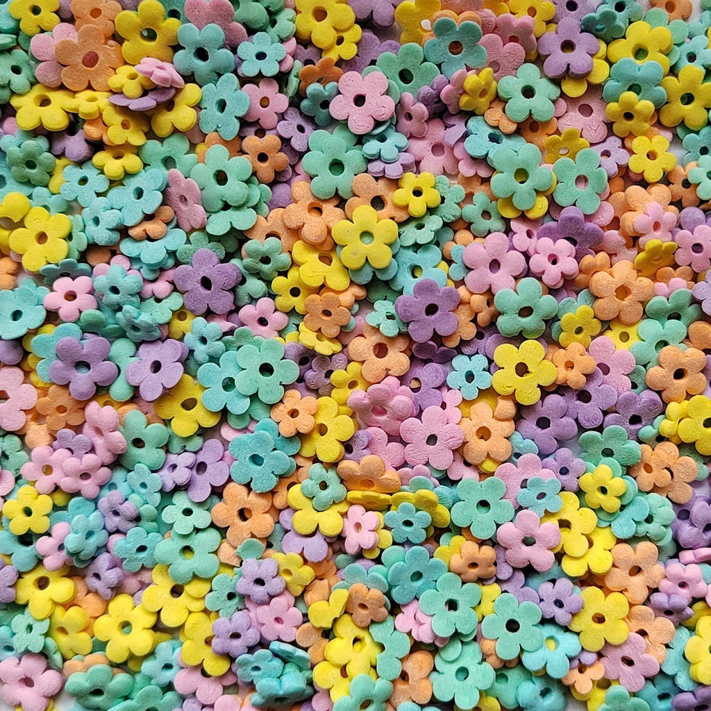 Assorted pastel edible flower-shaped sprinkles scattered across a surface, close-up view.