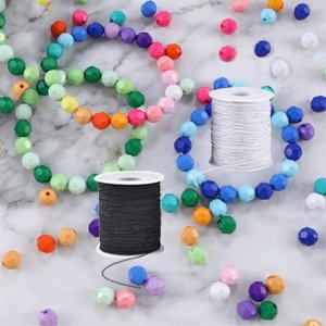 Two spools of elastic string, one black and one white, surrounded by colorful beads and partially finished bracelets on a marble surface.