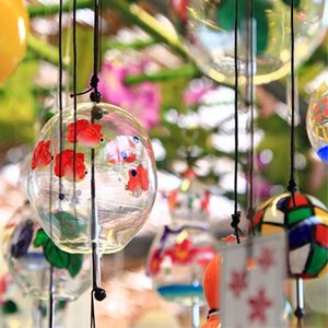 Close-up of several glass wind chimes with painted goldfish and floral designs, hanging outdoors with blurred foliage in the background.