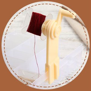 Embroidery floss organizer with a cream-colored bobbin winder and red thread on a plastic bobbin, inside a clear storage box.