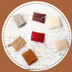 Embroidery floss wound onto plastic bobbins, arranged in a circle on a white textured surface.