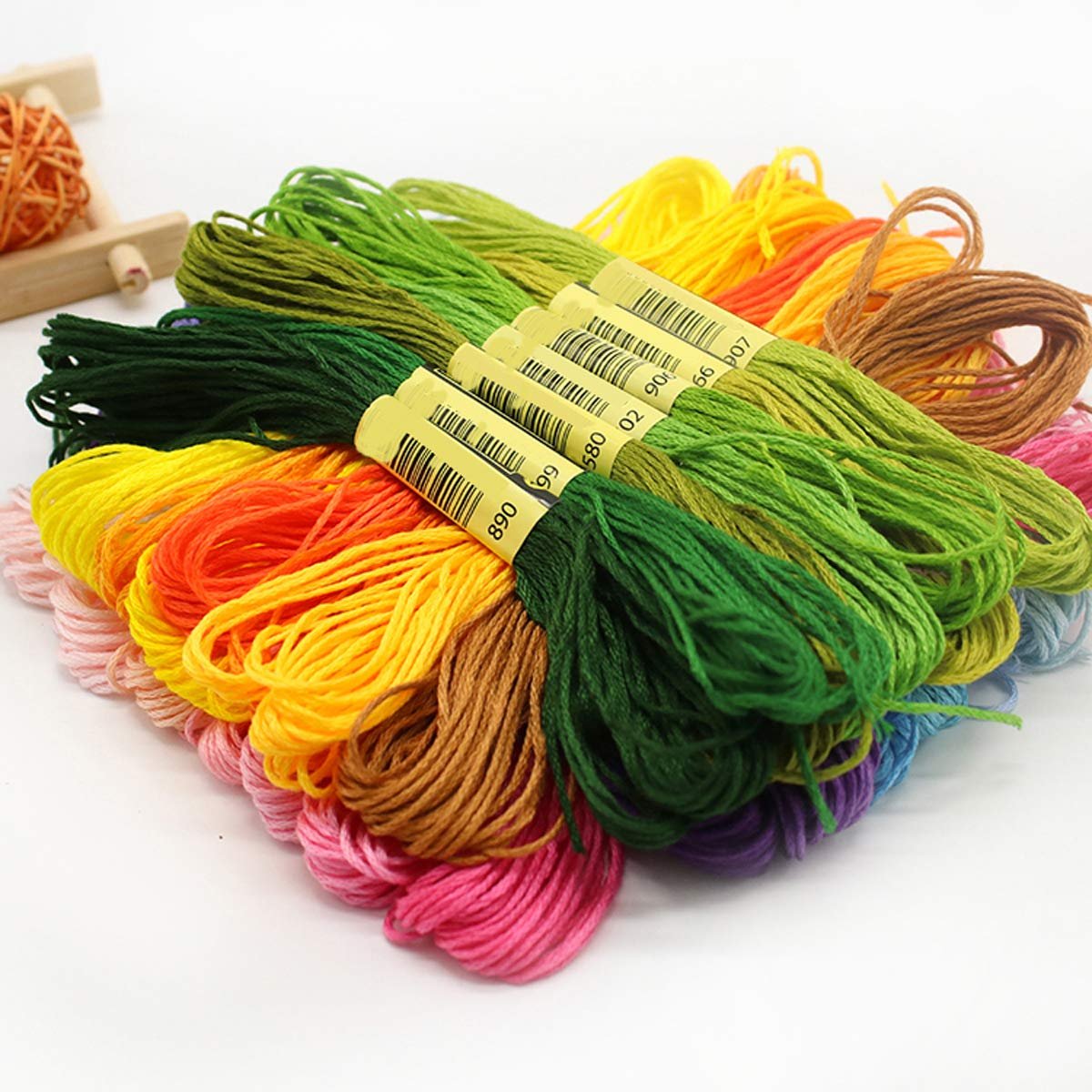 Pile of 50 rainbow-colored embroidery floss skeins with yellow color tags and barcodes, on a white background.
