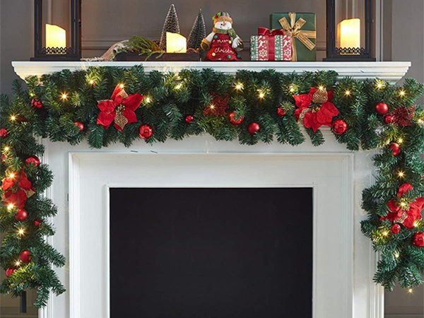 Christmas garland with lights and red poinsettias draped over a fireplace mantel, with decorative items on the mantel.