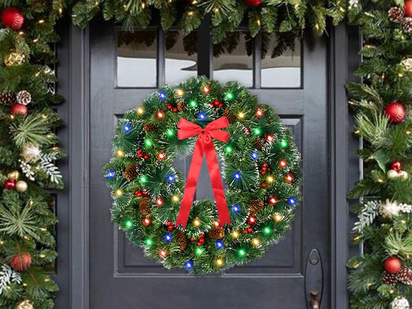 Lit Christmas wreath with red bow hanging on a dark door, flanked by garland.
