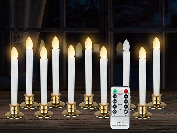Set of ten white LED taper candles with gold bases, arranged in front of a window, with a remote control.