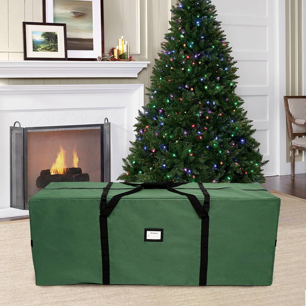 Green Christmas tree storage bag in a living room with a lit tree and fireplace