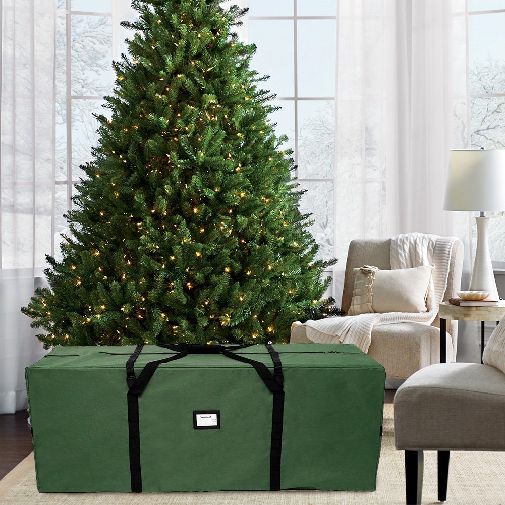 Green Christmas tree storage bag in front of a decorated artificial tree in a living room setting.