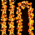 Autumn leaf garland with warm yellow LED string lights, double-layer maple leaf design, shown in a curved arrangement against a black background.