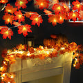 Autumn maple leaf string lights draped over a fireplace mantel with pumpkins and a candle lantern.