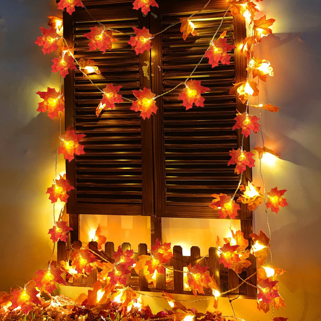 Fall maple leaf LED string lights draped across a wooden shutter and fence, illuminated with warm yellow light.