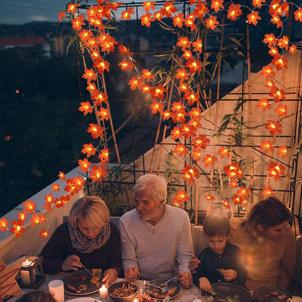 Family enjoying dinner on a balcony decorated with illuminated maple leaf string lights