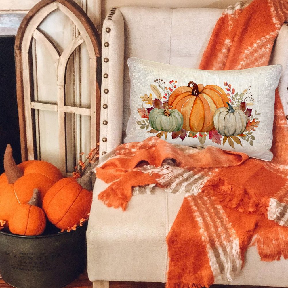 Lumbar throw pillow cover with watercolor pumpkins and autumn leaves design, on a chair with blankets.