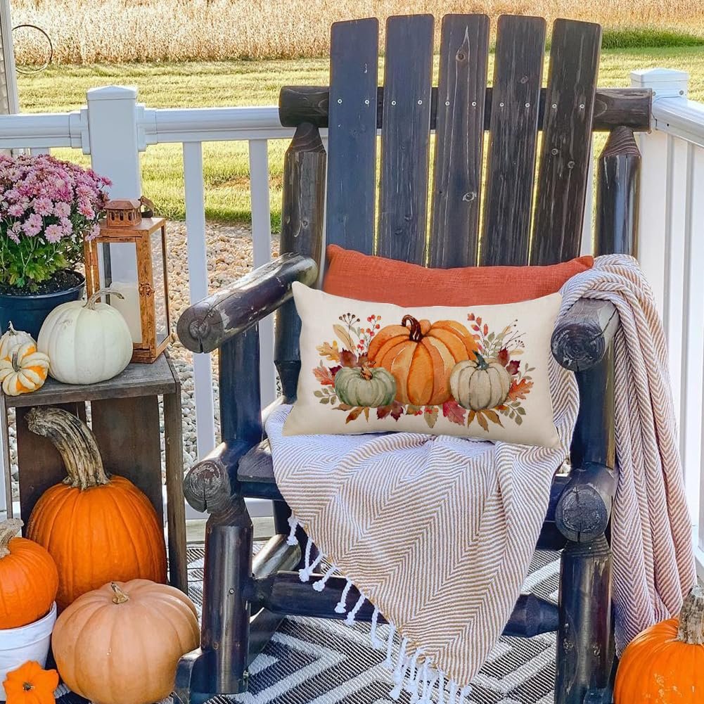 Lumbar throw pillow cover with a watercolor pumpkin and maple leaf design, displayed on a rocking chair with pumpkins and a blanket.
