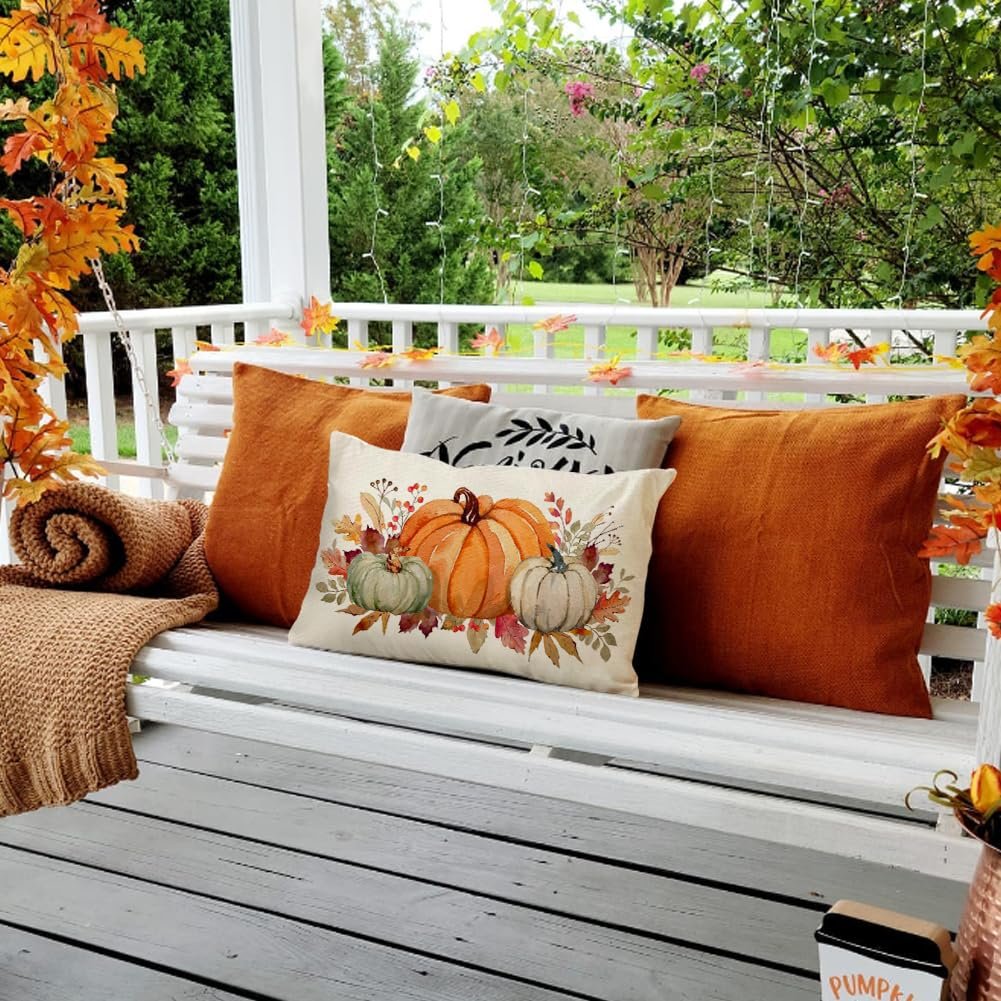 Lumbar throw pillow with pumpkins and maple leaves on a porch swing with orange pillows and a blanket.