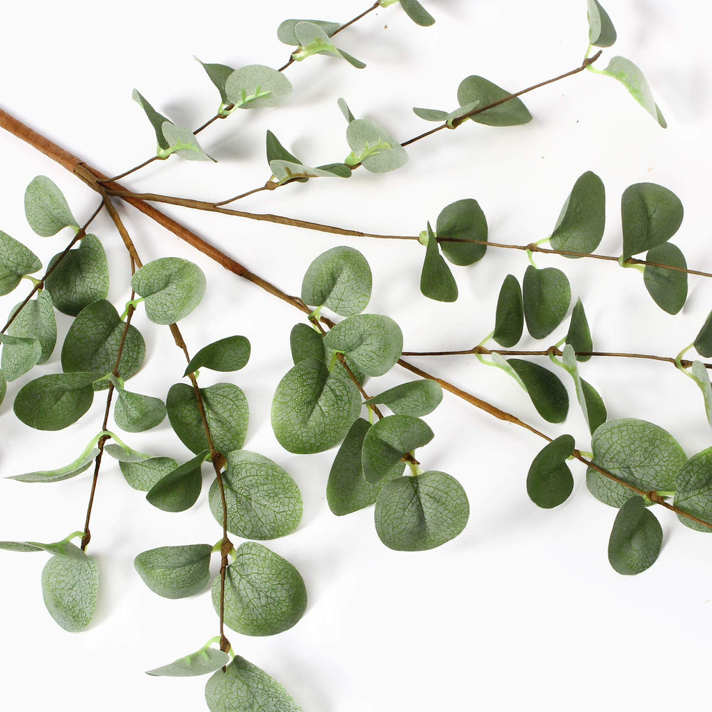 Faux eucalyptus stems with green leaves on a white background, close-up view