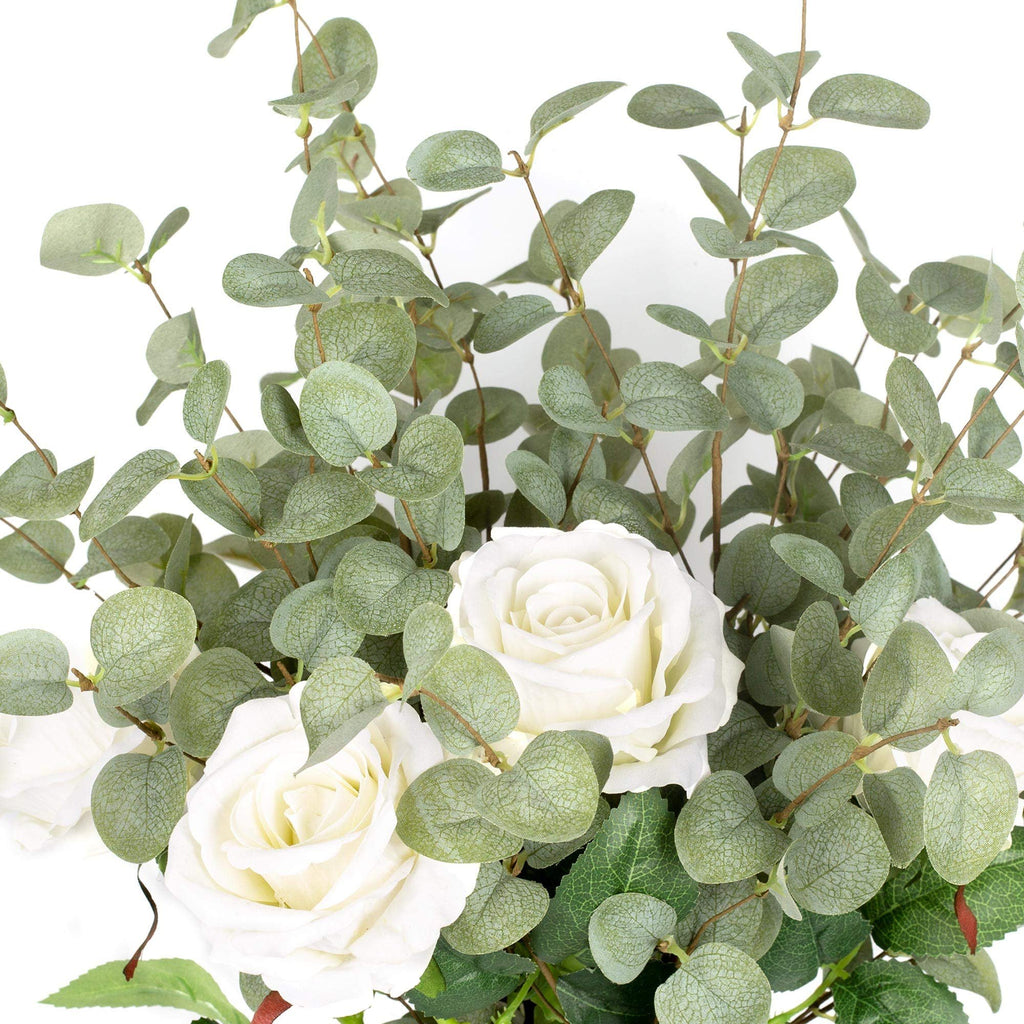 Close-up of faux eucalyptus stems with white roses against a white background.
