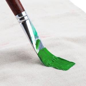 Flat paint brush with green paint on bristles, resting on a textured white surface.