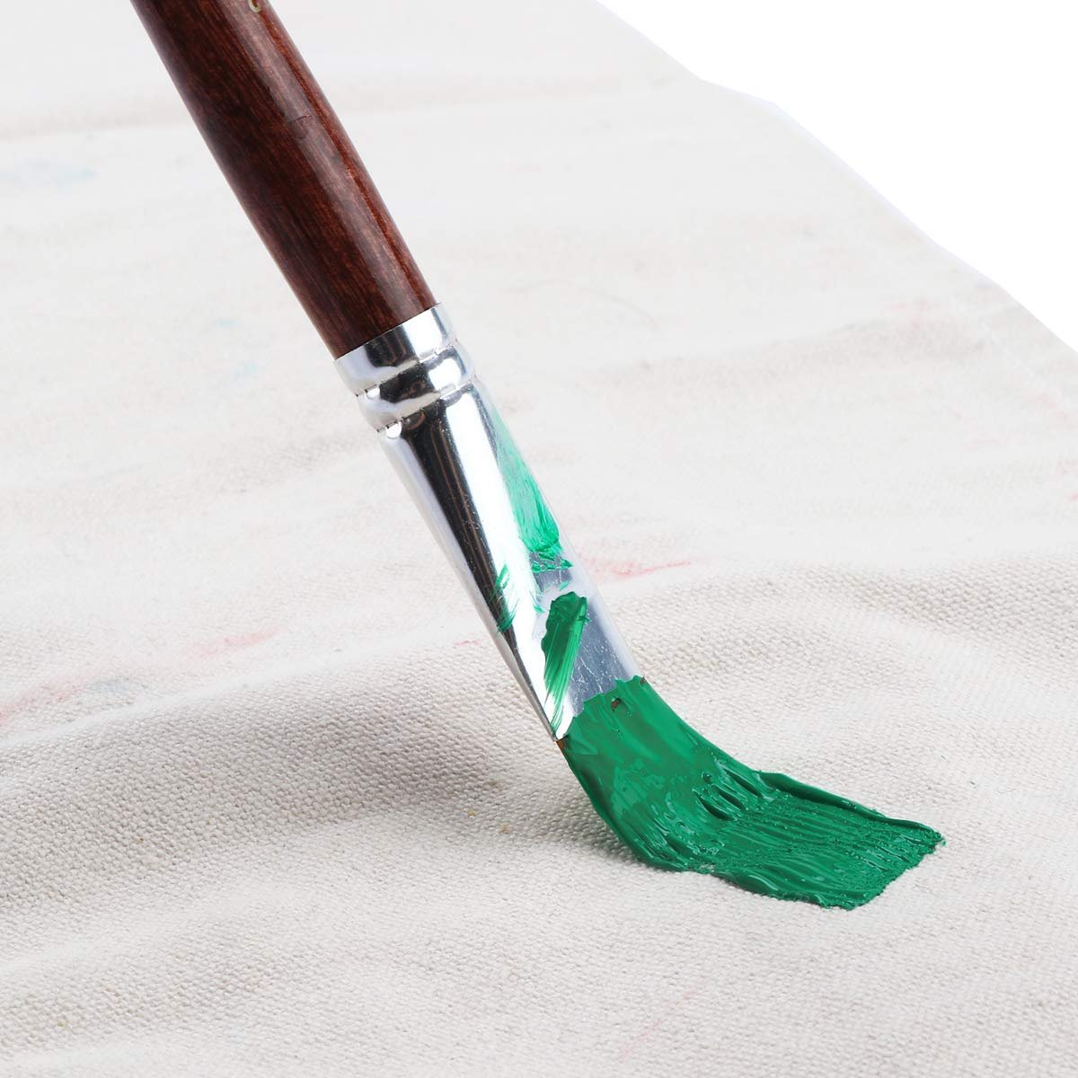 Flat paint brush with green paint on bristles, angled over textured fabric.