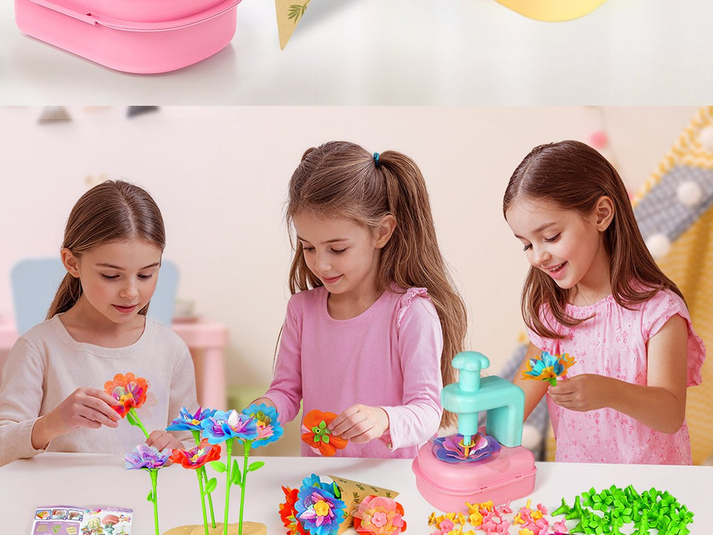 Three girls assembling colorful craft flowers with a pink and teal tool on a white table.