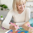 Woman and child smiling while working on a flower diamond painting kit at a table