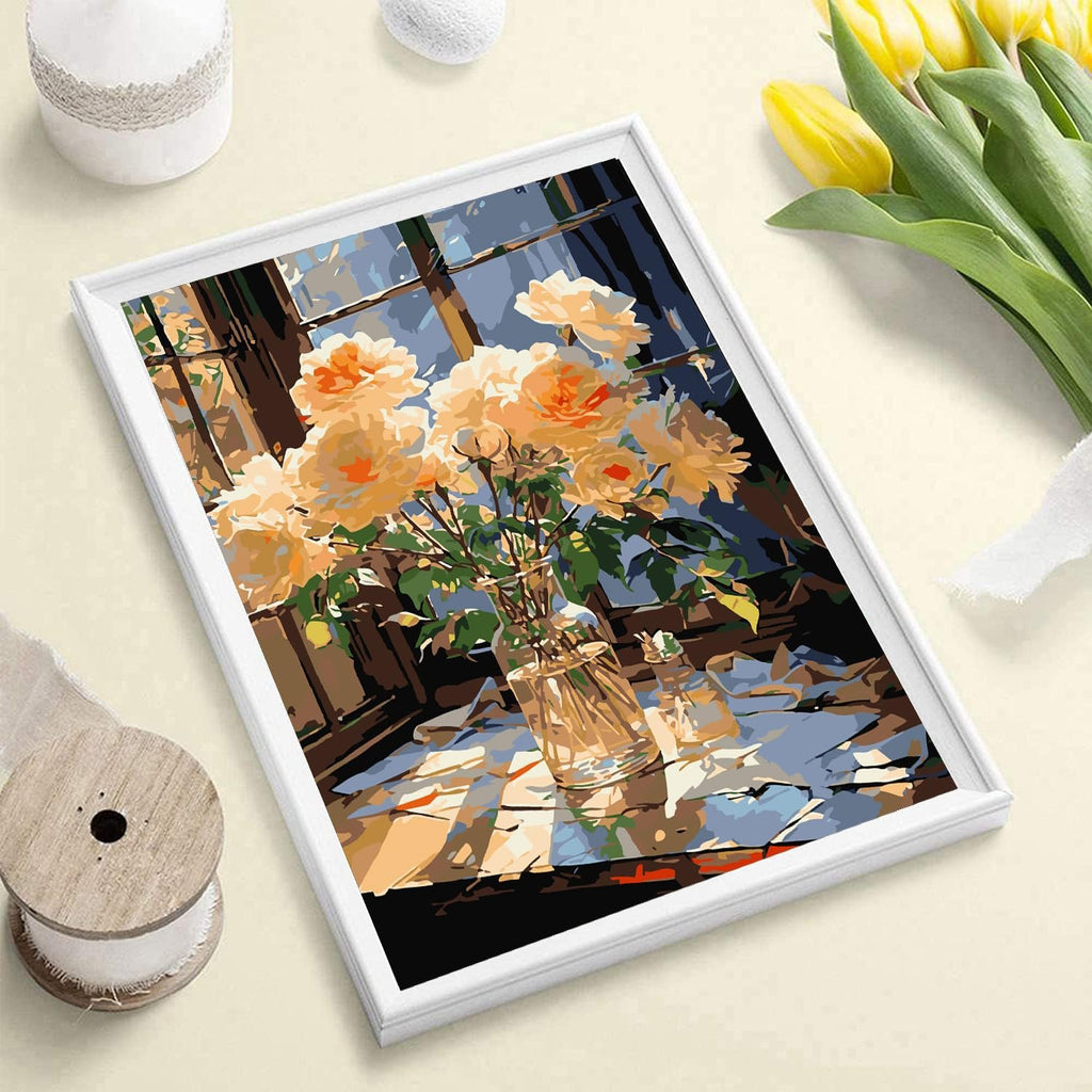 Paint by number artwork of a vase of yellow roses on a table by a window, framed in white.