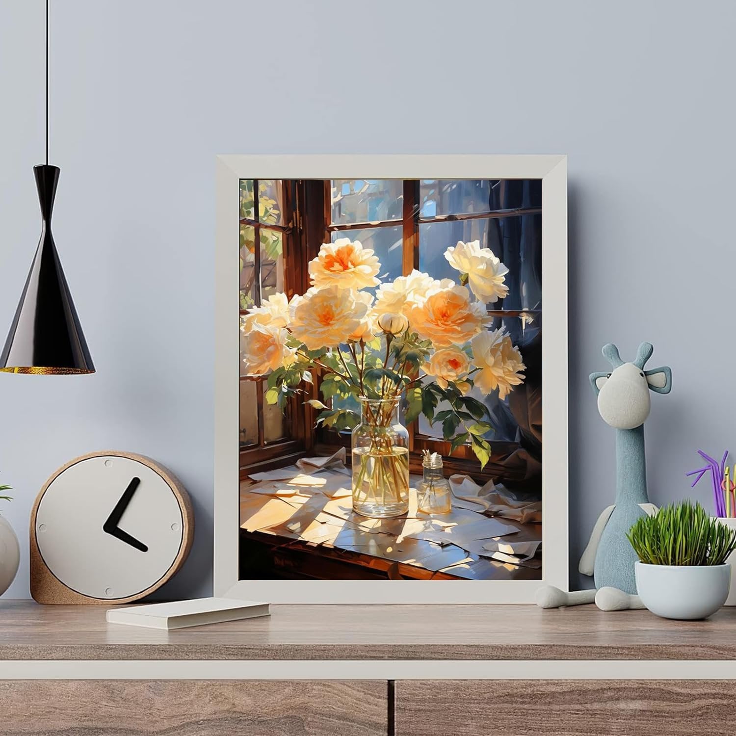Framed painting of yellow roses in a vase on a windowsill with scattered papers, displayed on a shelf with a clock and toy giraffe.