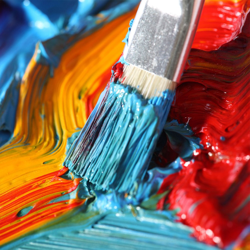 Paintbrush with blue paint mixing with yellow and red paint on a textured surface