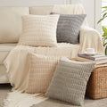Four decorative throw pillow covers in neutral tones arranged on a sofa with a throw blanket.