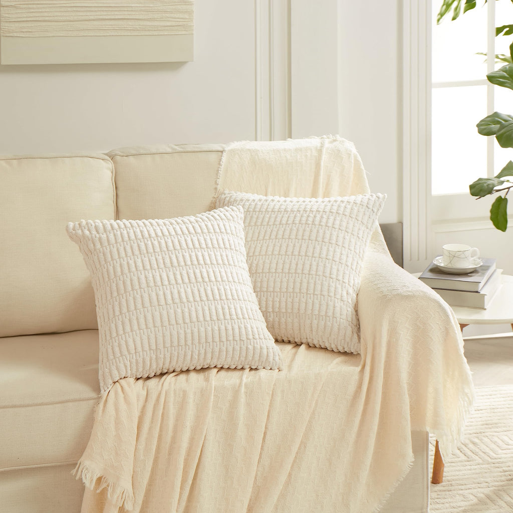 Two cream-colored textured throw pillow covers on a sofa with a cream throw blanket.