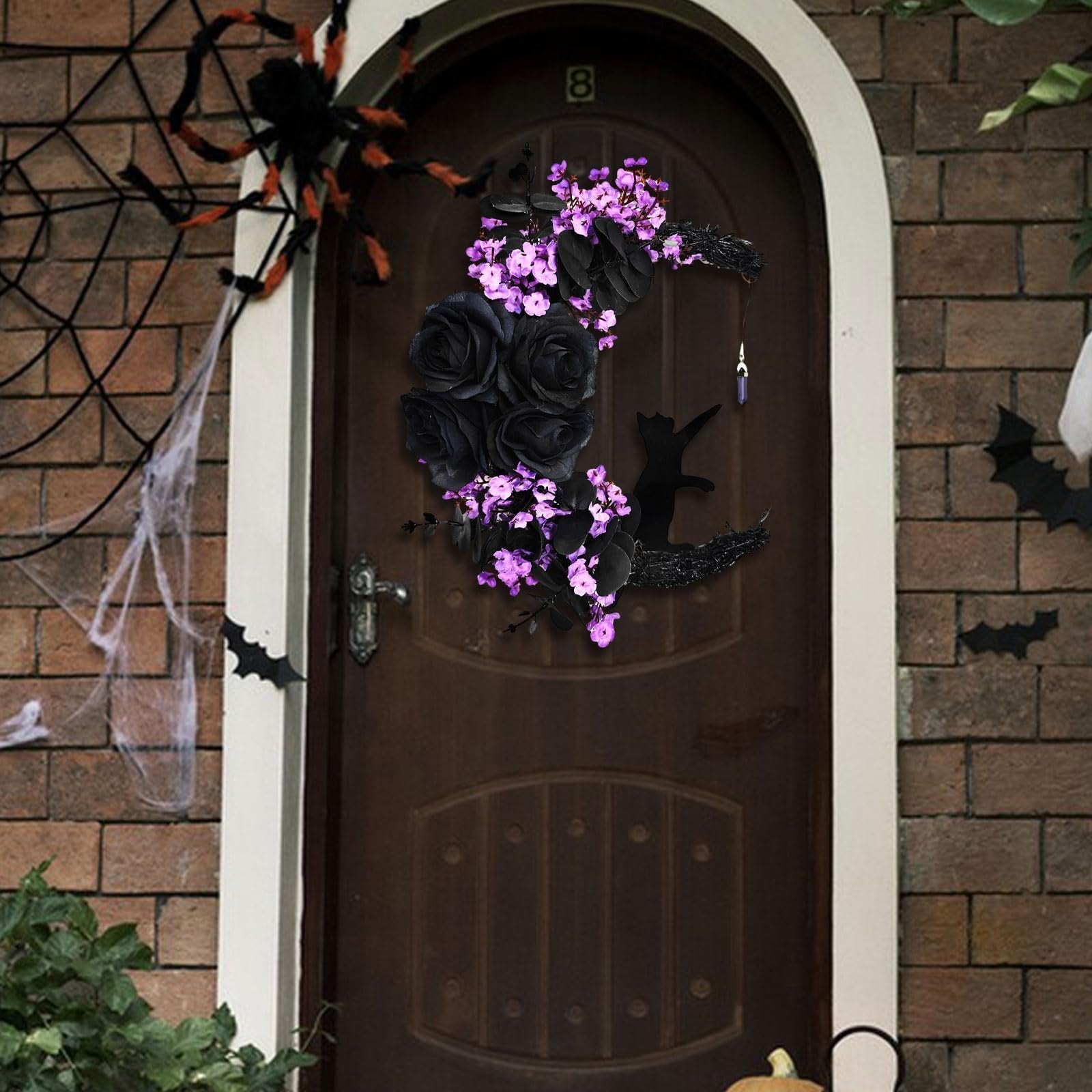 Halloween moon wreath with black roses, purple flowers, and a black cat silhouette hanging on a dark wooden door with spiderweb and bat decorations.