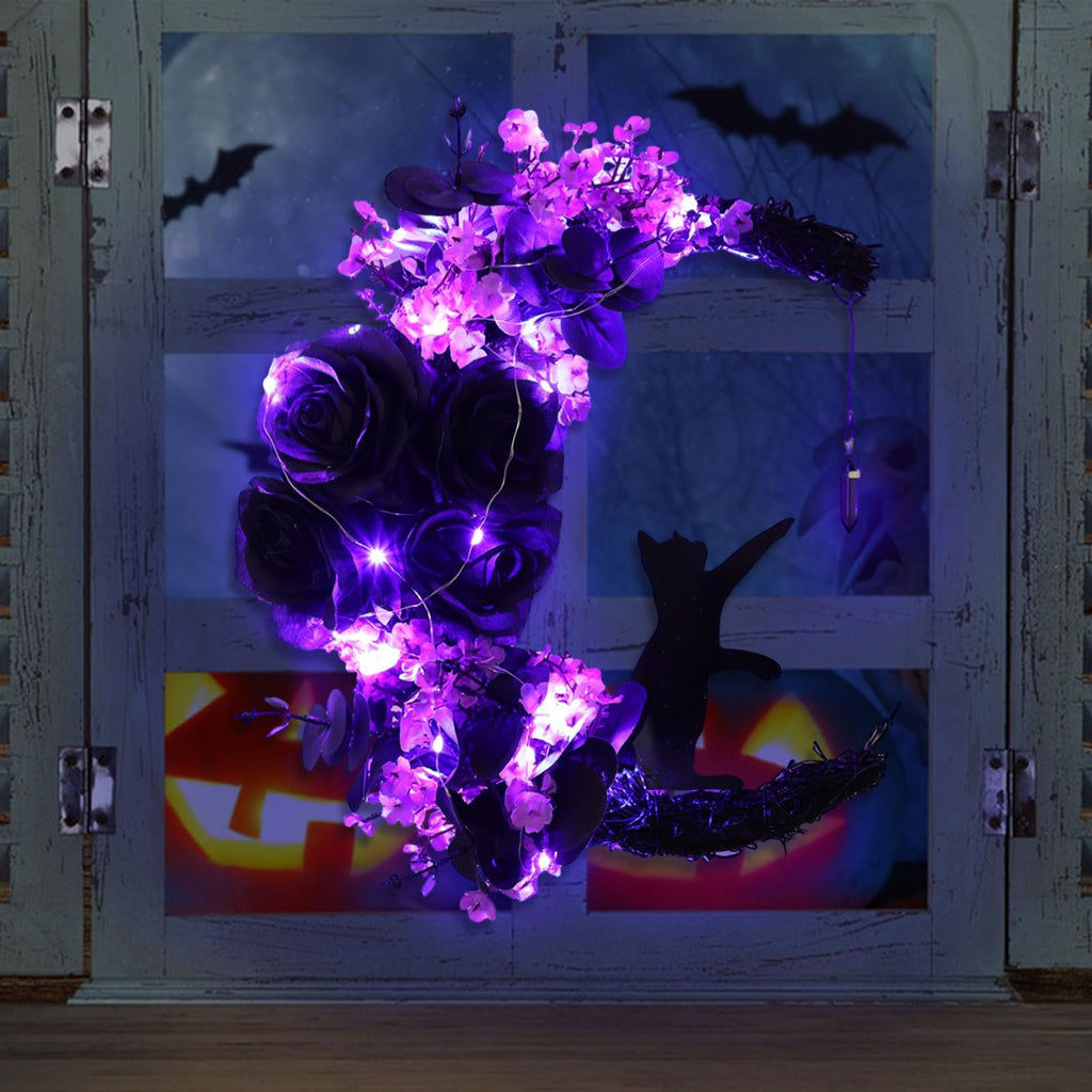 Crescent moon Halloween wreath with black cat, purple flowers, greenery, and LED lights, displayed on a window with spooky background.